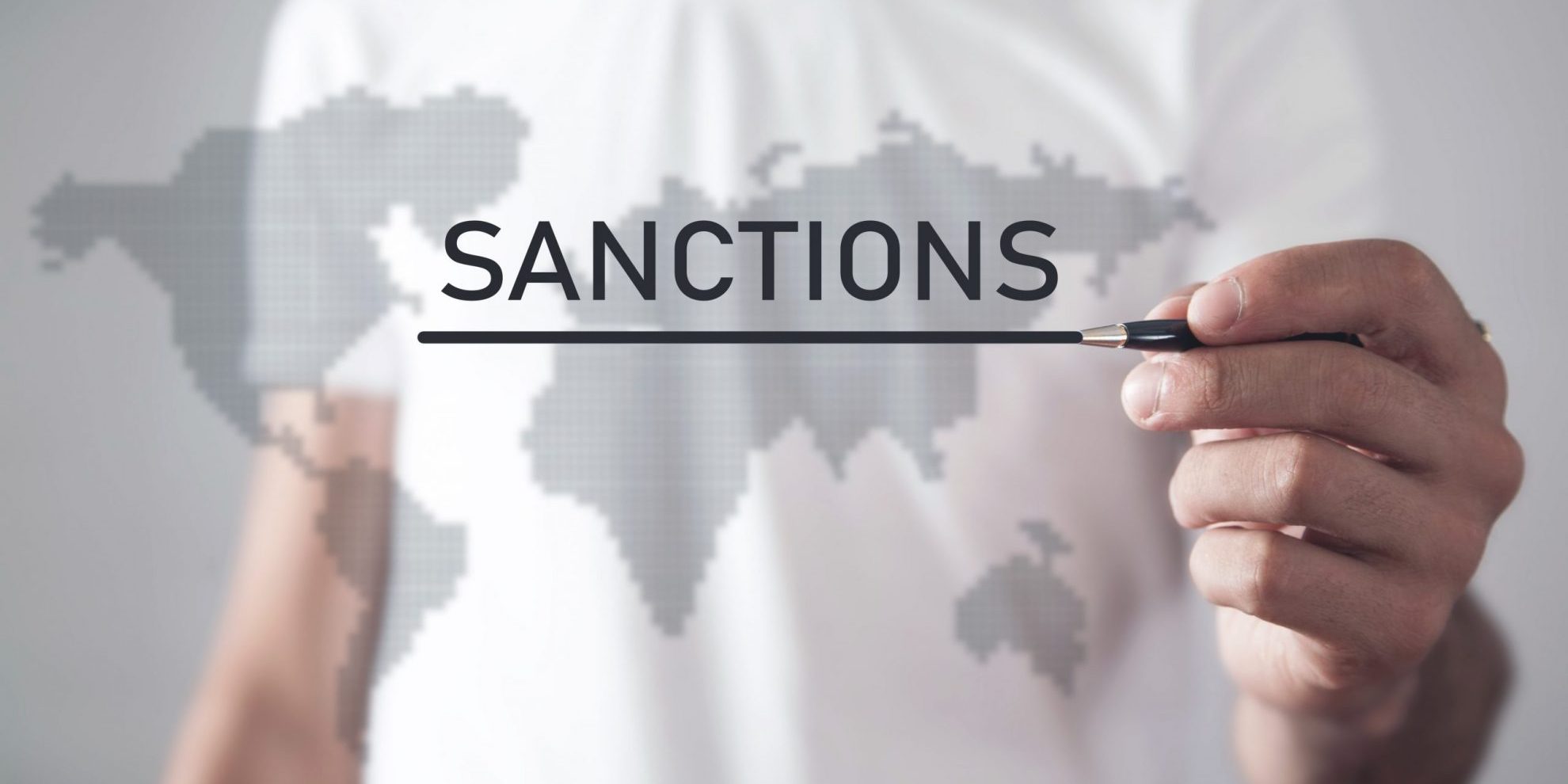 Photo of man writing the word "Sanctions" on a translucent map illustratees blog: "What Are OFAC Sanctions?"