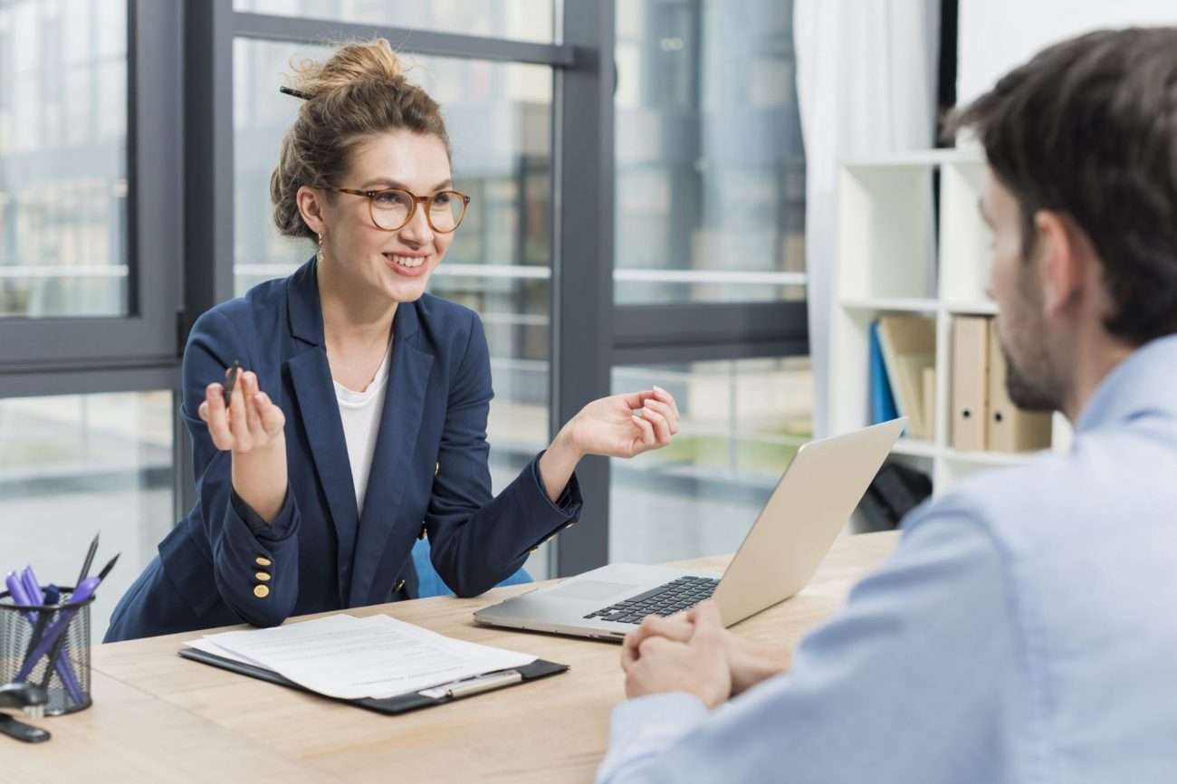 Photo of woman with glasses talking to man seen from behind illustrates blog: "4 Common Interview Mistakes Hiring Managers Make"
