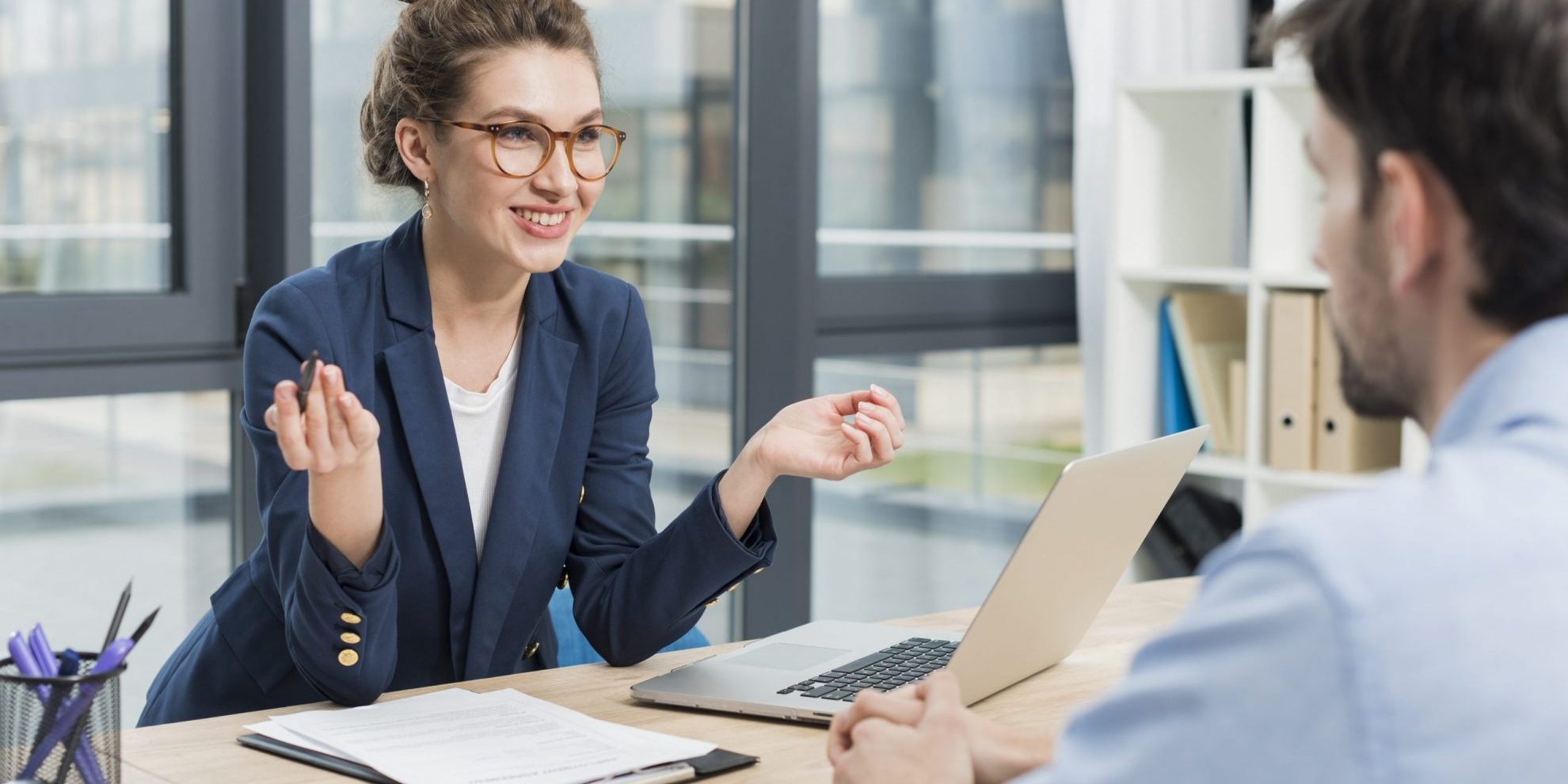 Photo of woman with glasses talking to man seen from behind illustrates blog: "4 Common Interview Mistakes Hiring Managers Make"