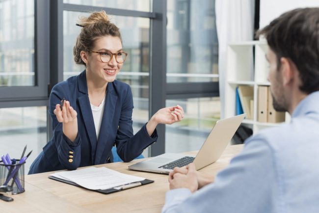 Photo of woman with glasses talking to man seen from behind illustrates blog: "4 Common Interview Mistakes Hiring Managers Make"