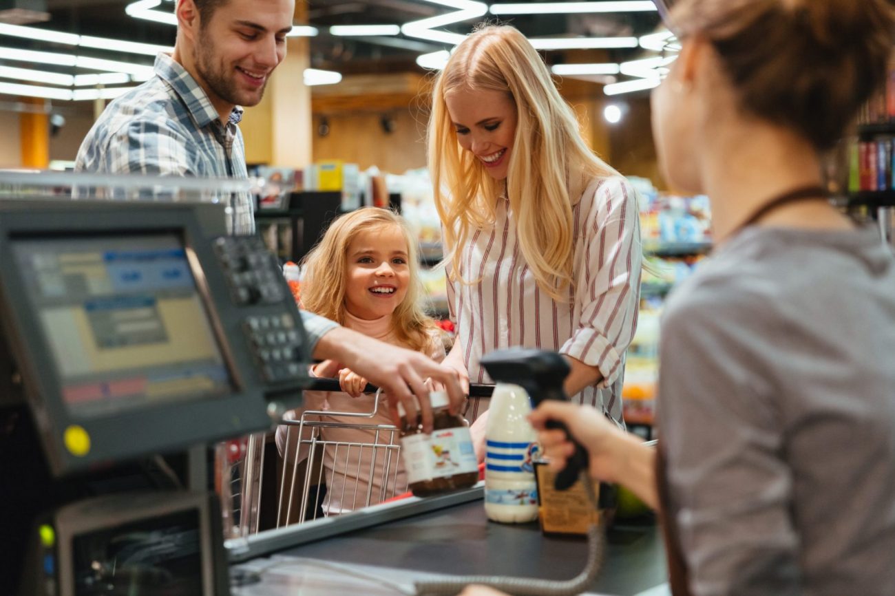 Photo of family at supermarket checkout counter with employee scanning items illustrates blog: "Background Checks for Retail Jobs: Here’s Why They Matter"