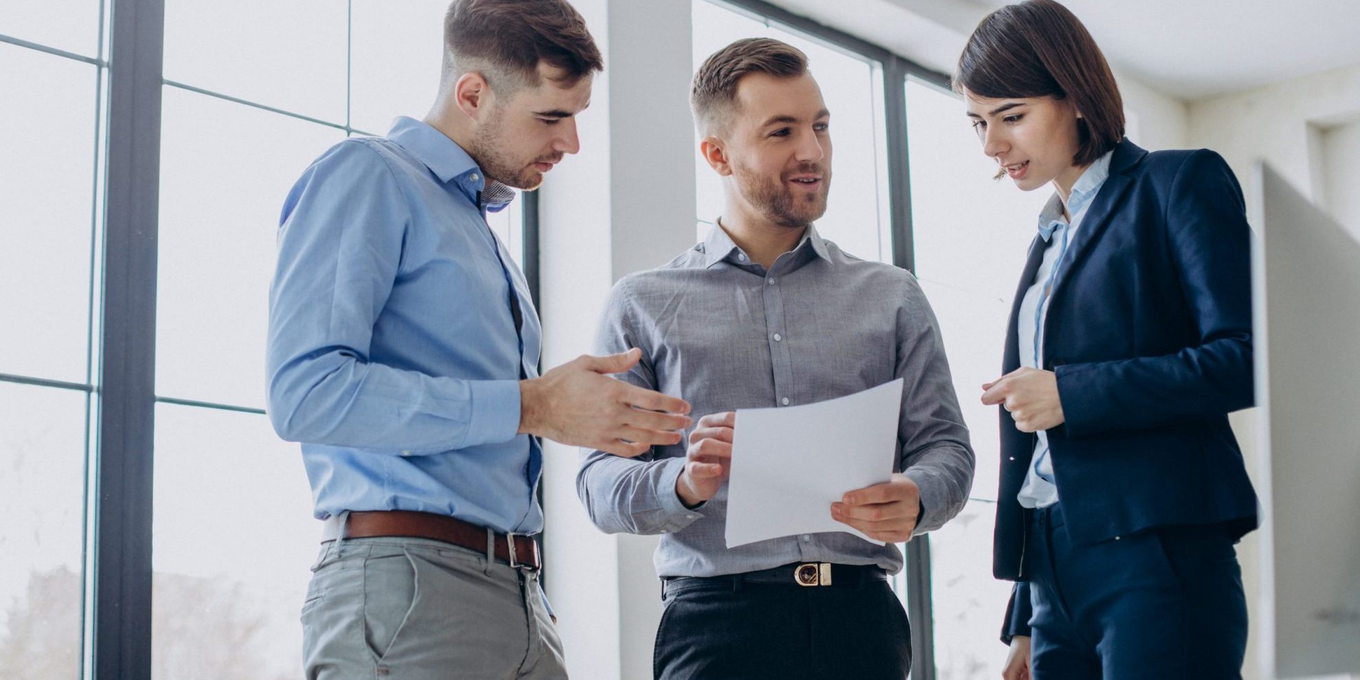 Three executives talking holding sheets of paper.