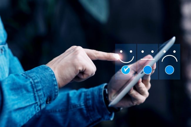 BrandReputation Closeup of man holding tablet with overlay of smiley face, neutral face, and sad face illustrates blog "What Is Brand Reputation and Why It Matters"