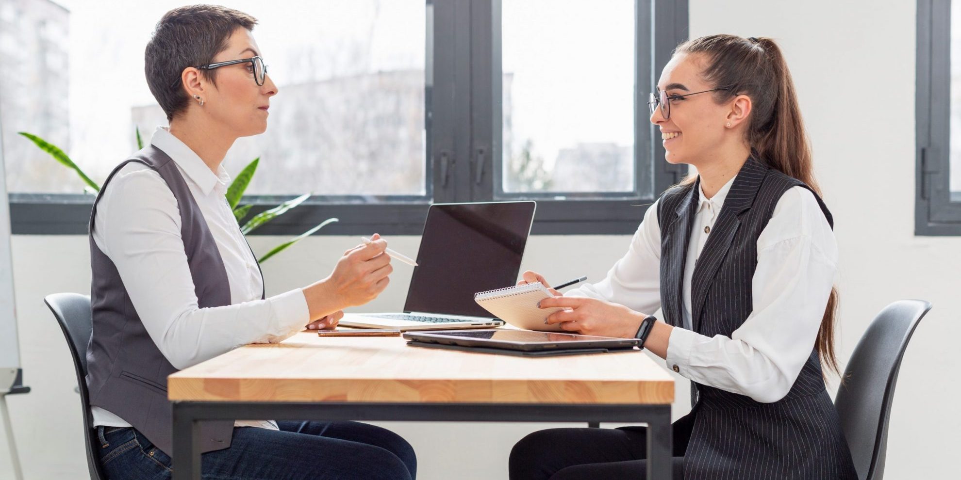 JobInterview7-FP Two women sitting at desk talking illustrate blog "How to Use Active Listening When Conducting a Job Interview"