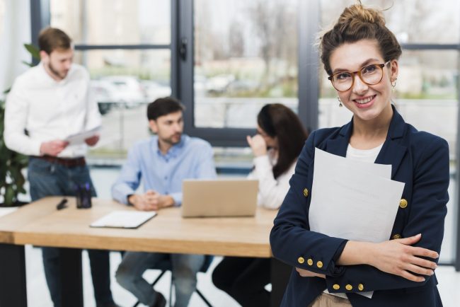 resume-jobs-FP Woman in business attire with people sitting at desk in the background illustrates blog "Will a Background Check Show All My Jobs?"