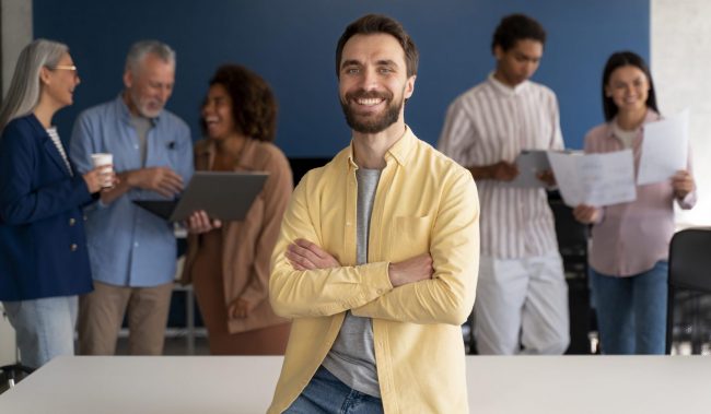 employer-employee-fp Man sitting on desk with people in the background illustrates blog "When To Run Background Checks?"