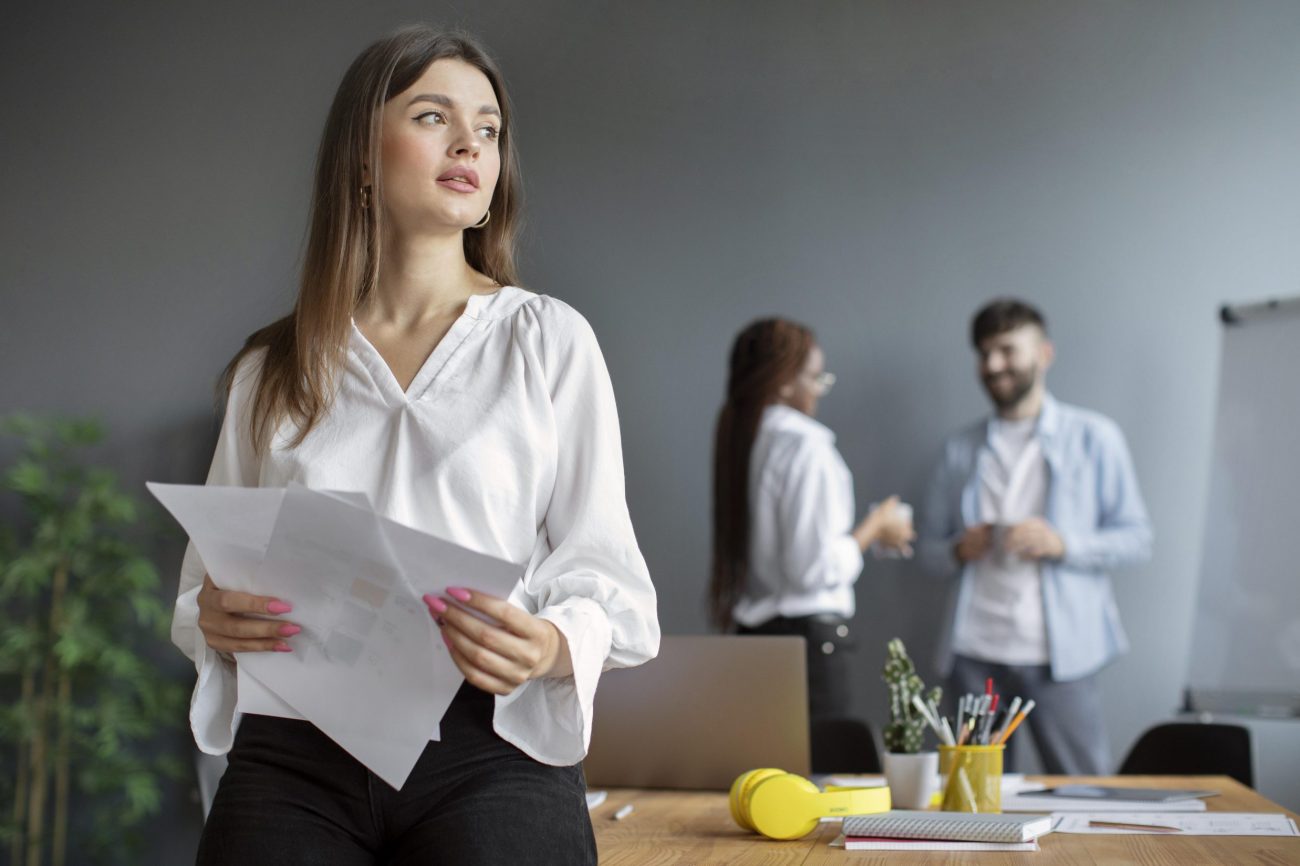 office-woman-fp Woman in office with man and woman in the background illustrates blog "What Is Performance Management?"