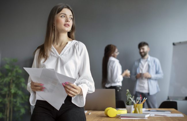 office-woman-fp Woman in office with man and woman in the background illustrates blog "What Is Performance Management?"