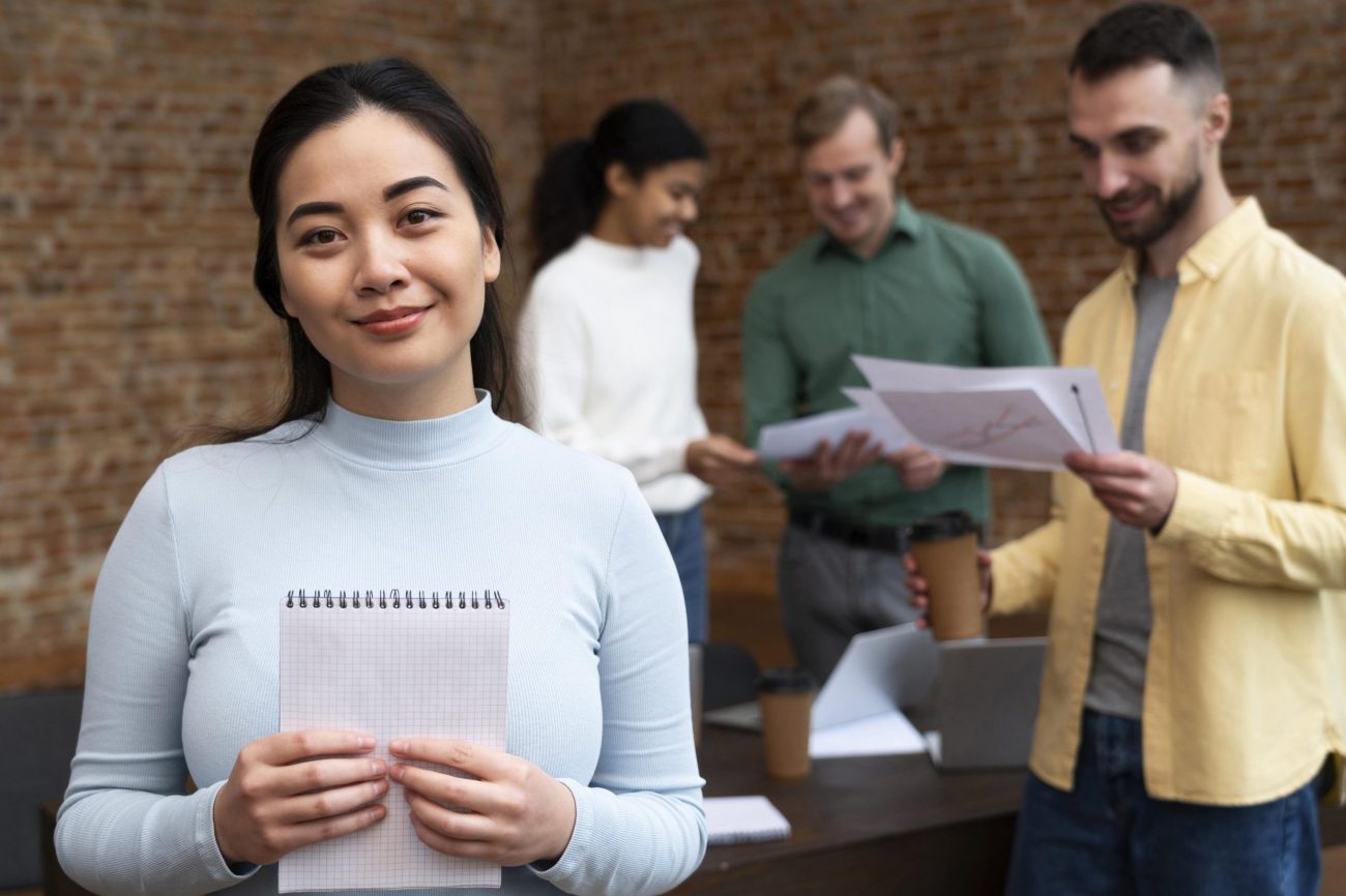job-candidates-fp Woman holding notebook with people in the background in office.