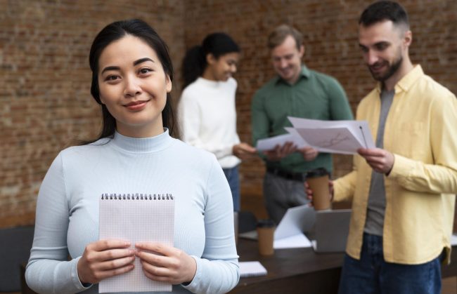 job-candidates-fp Woman holding notebook with people in the background in office.